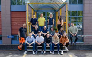 15 people sitting in front of an office building.