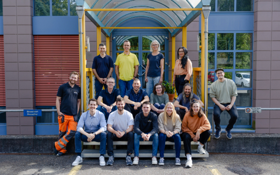 15 people sitting in front of an office building.